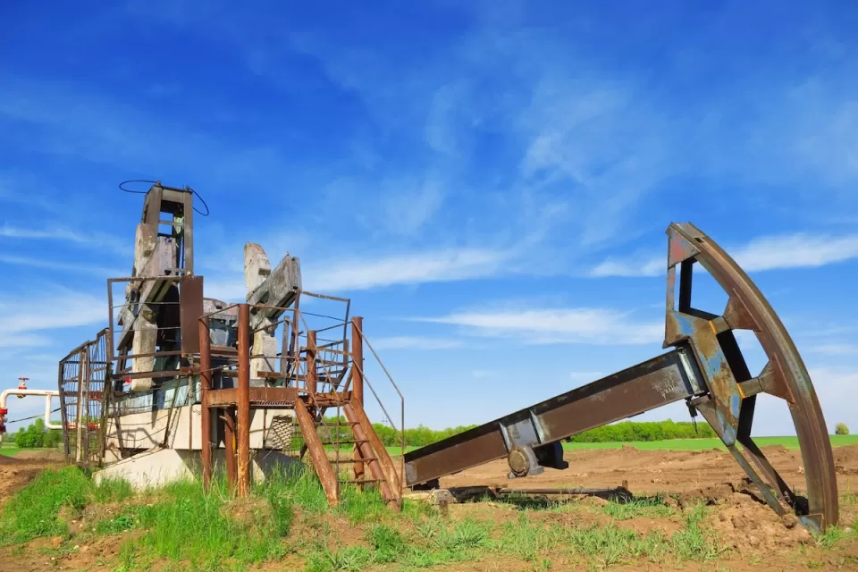 Defunct oil well disassembled in green field.